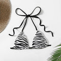 The Zebra Noir Padded Halter Bikini Top in stylish zebra print with black ties and a tropical backdrop.